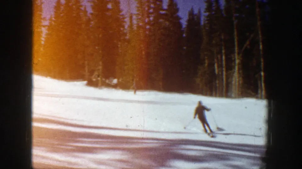 Distant skier on a sunlit Aspen slope in 1961, framed by dark evergreen trees and warm film color.