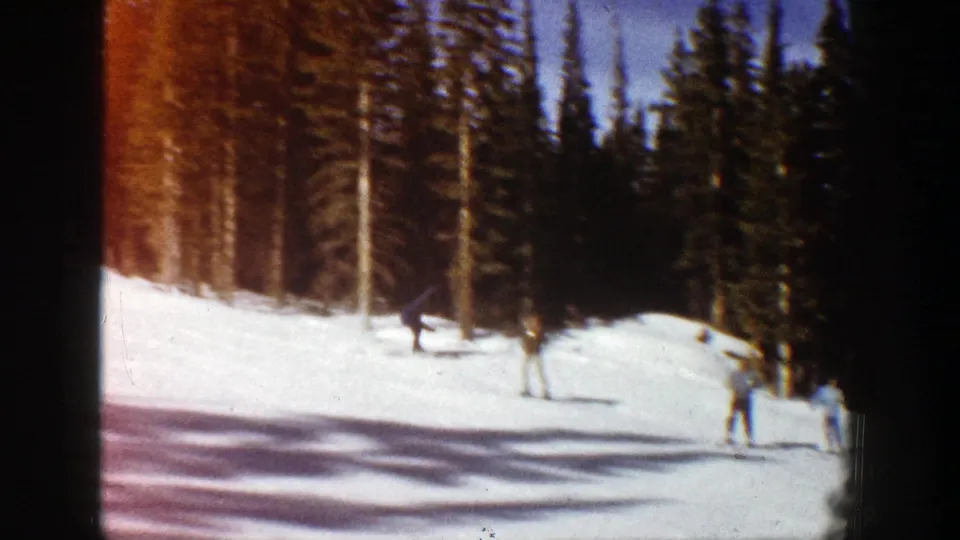 Aspen, Colorado 1961 frame showing several skiers on a bright slope beneath evergreen trees.