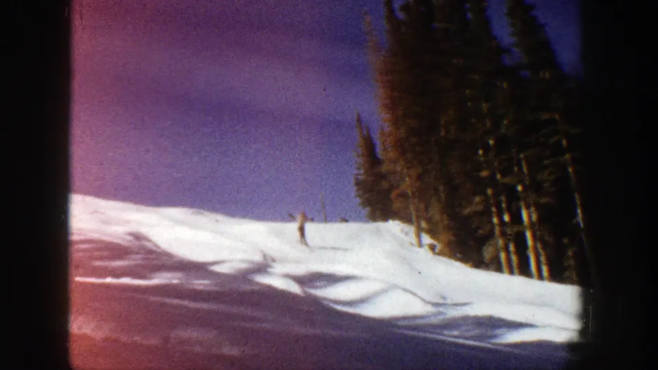A distant skier moves across a snowy Aspen, Colorado slope in 1961, with evergreen trees and visible 8mm frame edges.