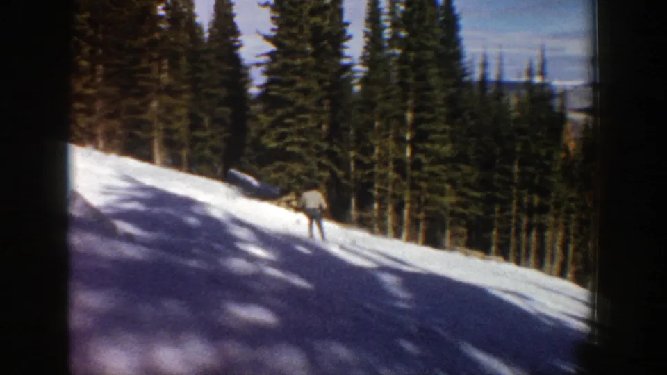 Distant skier on a snow-covered Aspen hillside in 1961, framed by tall conifers and 8mm film borders.