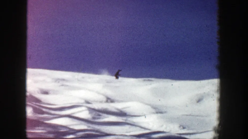 A small skier crosses an open snowy rise in this 1961 Aspen 8mm frame, with soft grain and visible film edges.