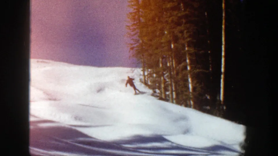The skier carves down the Aspen slope, with evergreen trees at right and visible 8mm color shift along the frame.