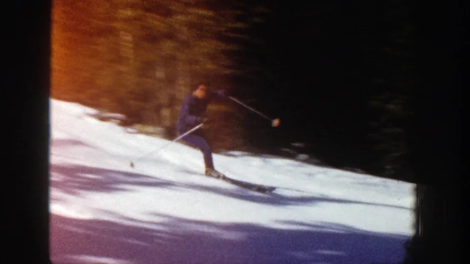 1961 Aspen, Colorado home-movie frame of a skier on snow beside dark evergreens, with a warm orange and purple light leak across the image.