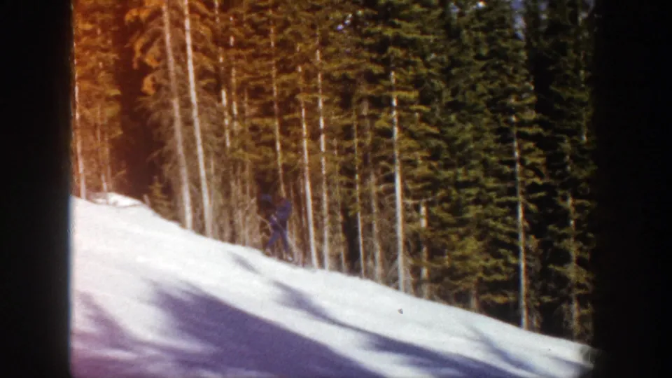 1961 Aspen home-movie frame showing a distant skier moving along a snowy forested slope under winter light.