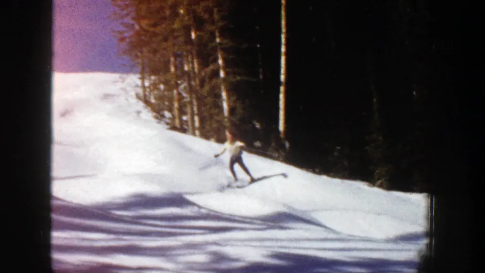 A skier descends near the forest edge in 1961 Aspen footage, with ski poles visible against sunlit snow.