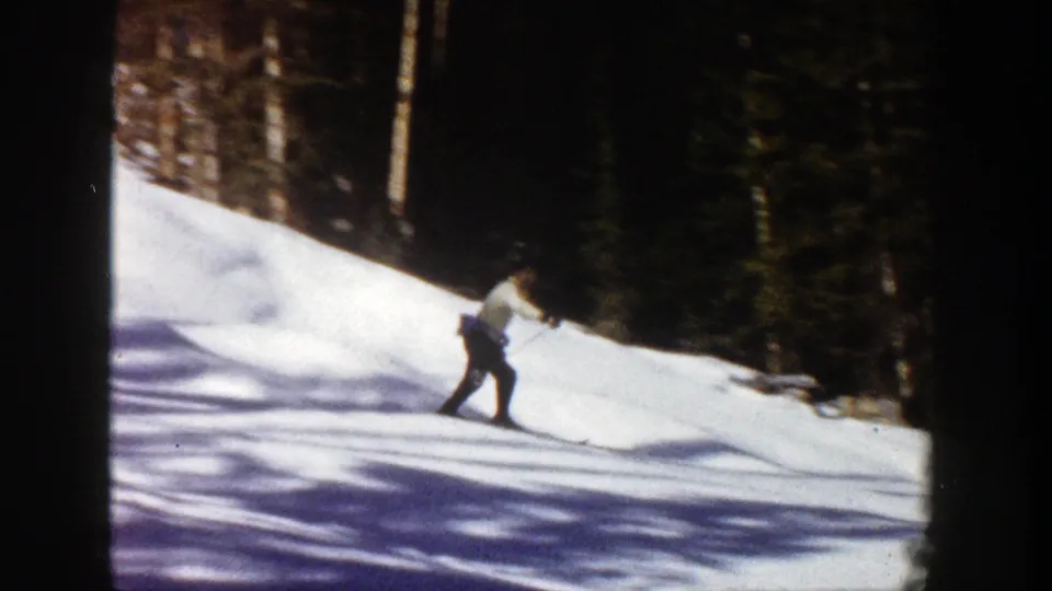 The skier continues across the 1961 Aspen ski slope, with bright snow and evergreen forest filling the frame.