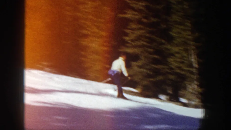 A distant skier in Aspen, Colorado turns along the snowy run, with warm film color and shadowed evergreens behind.