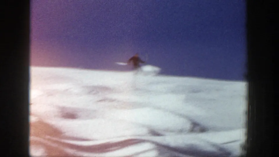 A soft, distant frame shows the skier cresting or descending a snowy rise in the 1961 Aspen home-movie footage.