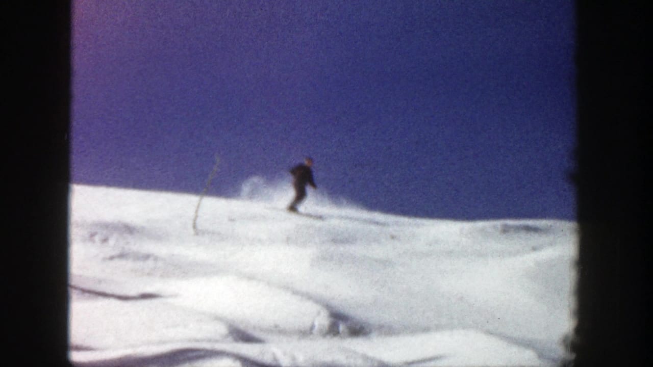 A distant skier in dark clothing moves across an Aspen, Colorado snow slope in 1961 home-movie footage.