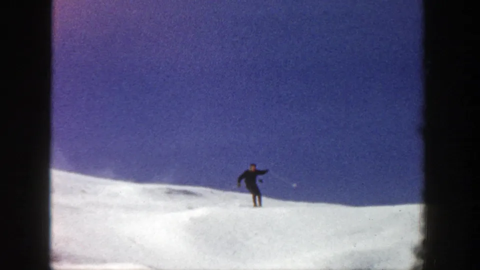 The skier appears small against the open Aspen snowfield, turning near the crest under a clear blue sky.