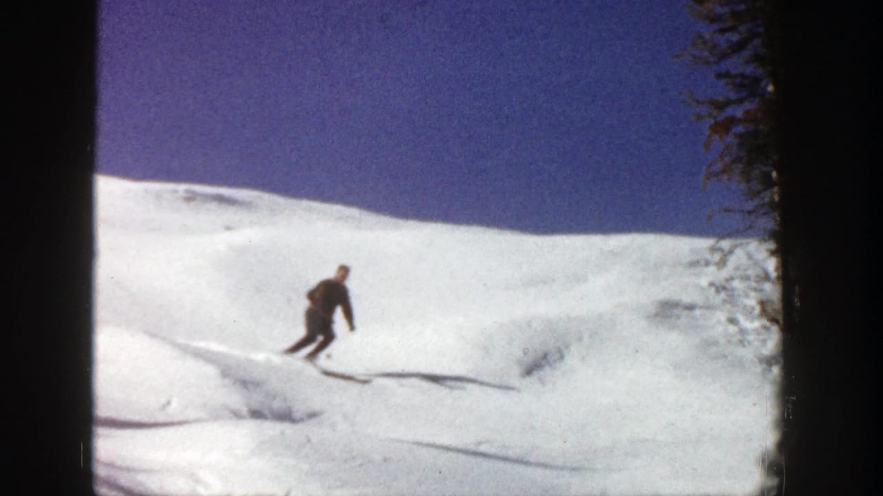 A distant skier moves across a white Aspen snow slope in 1961 home-movie footage, with trees at the edge of the run.
