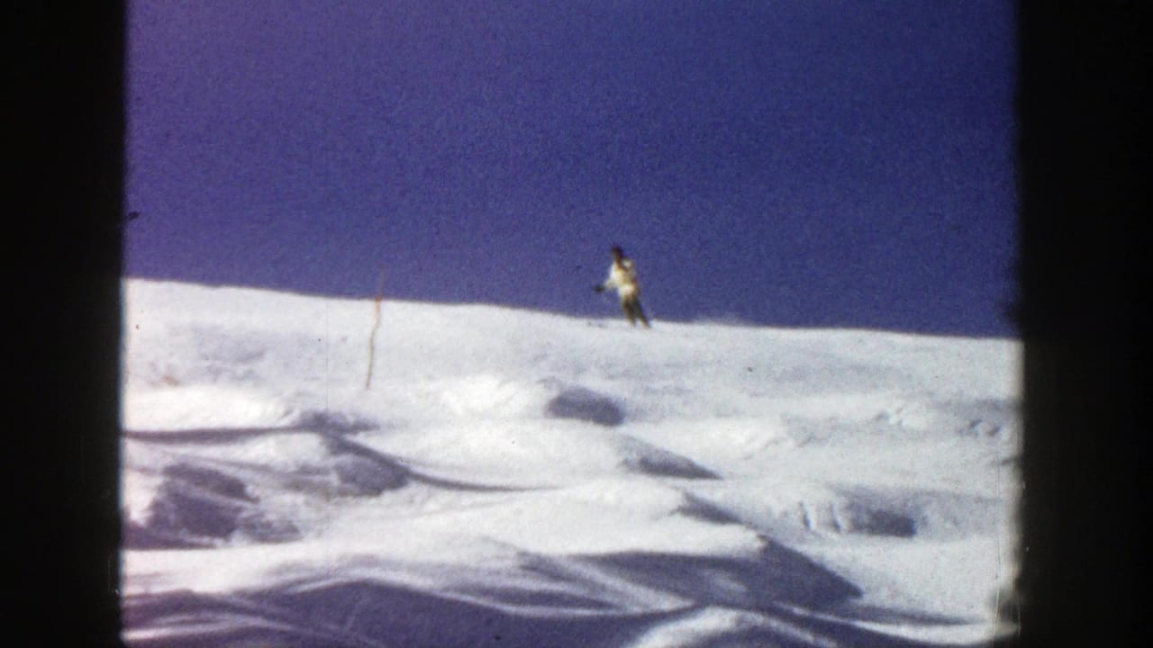 Distant skier standing or beginning to move along a snowy ridge under a deep blue sky.