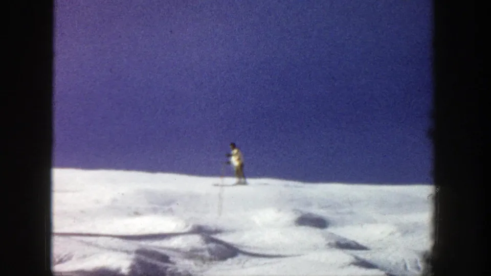 A distant skier traverses an open Aspen snowfield in this 1961 8mm frame, with tracks visible across the slope.