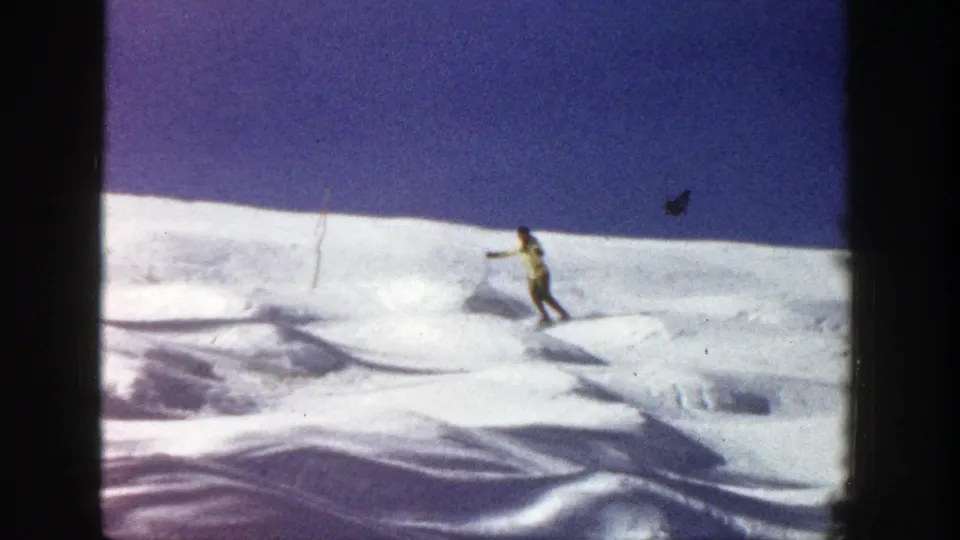 A skier in a light jacket moves across rolling snow in Aspen, Colorado, with ski poles visible against the blue sky.