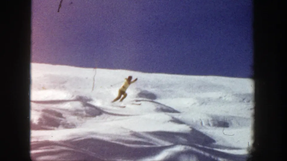 The skier leans downhill on a sunlit Aspen snow slope, with low drifts and soft 8mm color visible in the frame.