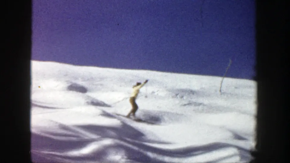 A lone skier continues across the uneven Aspen snowfield, framed by dark contact-sheet borders and a clear blue sky.