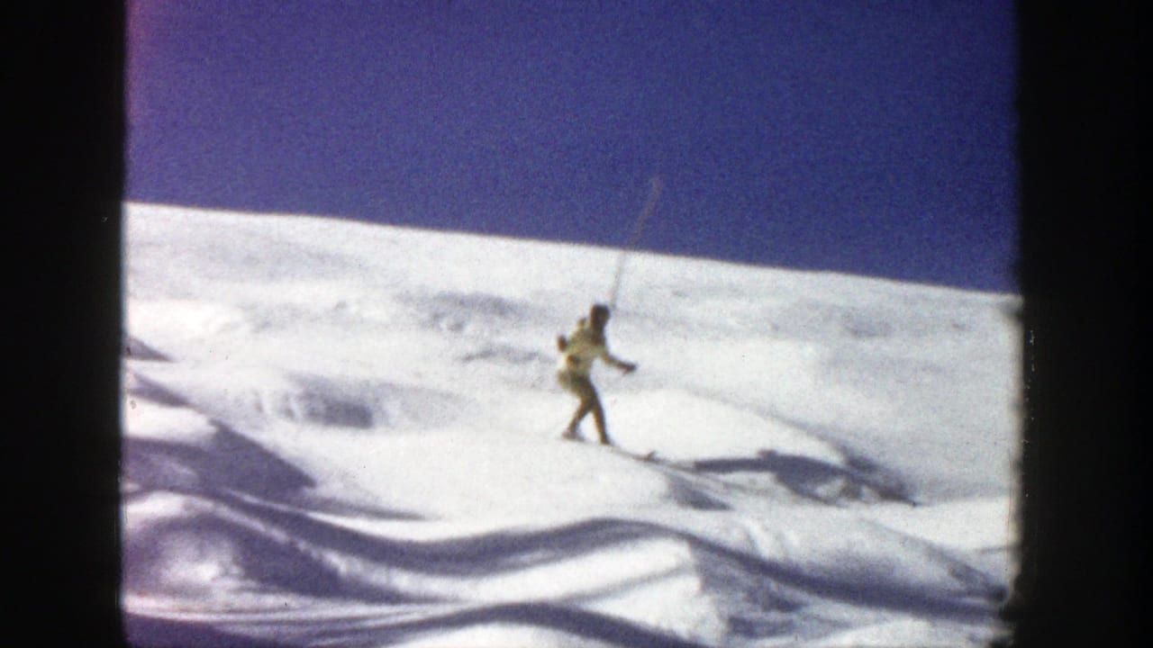 Skier in a yellow jacket crosses a snowy slope under a dark blue sky.