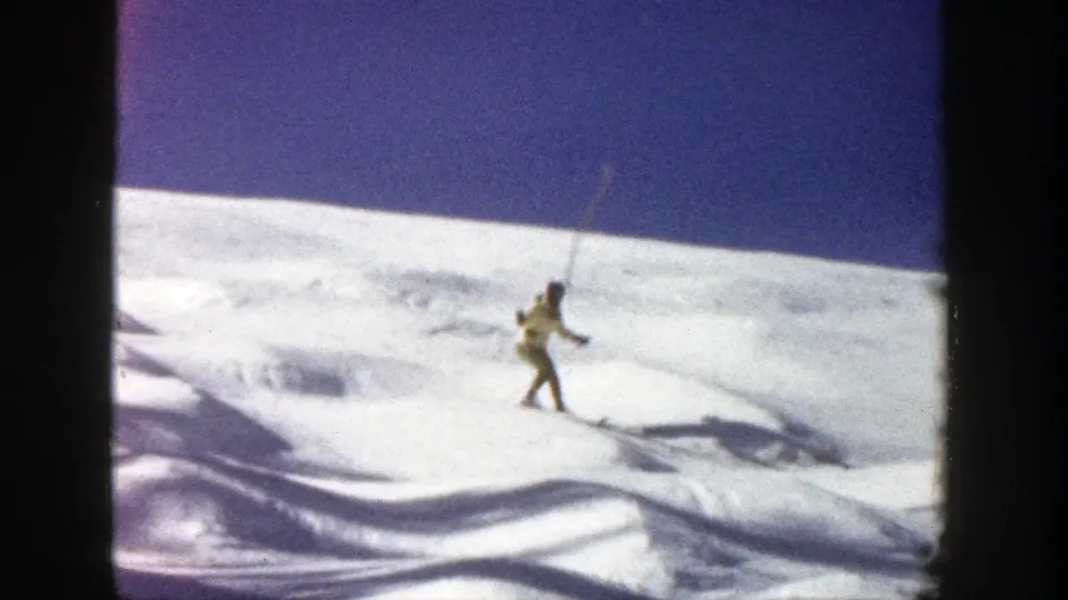 Adult skier in Aspen, Colorado, 1961, moves across rolling snow with poles and narrow skis visible.