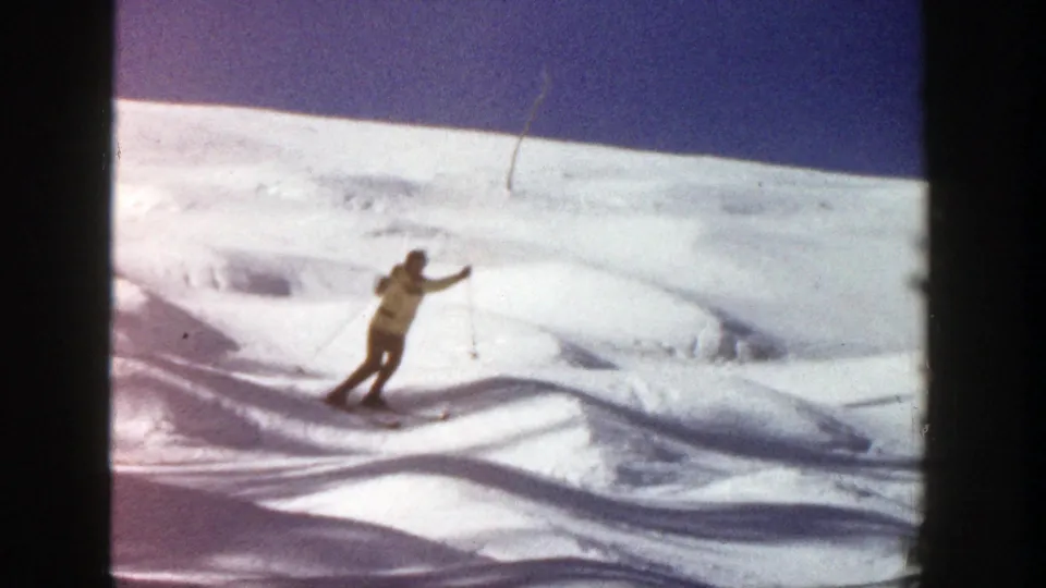 Adult skier in a yellow jacket makes a short turn on a snowy Aspen slope, with film grain and color shift visible.