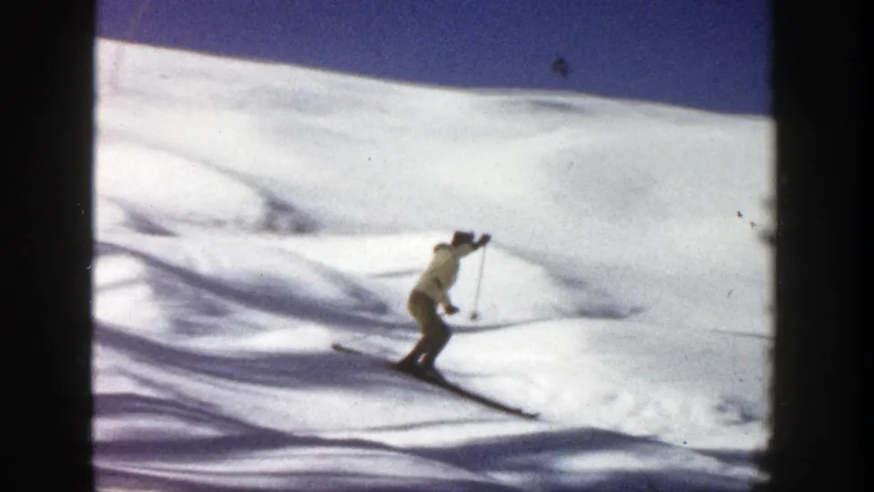 Adult skier approaches the foreground on narrow skis, using poles while descending the Aspen slope in 1961 footage.