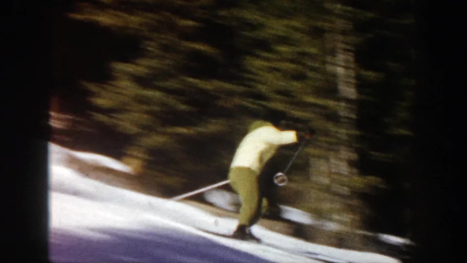 The woman in yellow ski clothing leans forward while moving past evergreen trees on a snowy Aspen slope, captured with handheld motion blur.