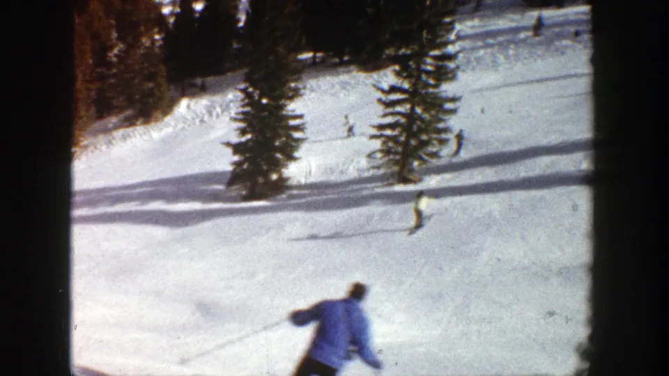 1961 Aspen ski frame with a blue-jacketed skier close to camera and several smaller skiers spread across the sunny slope.