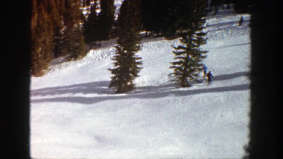 Near the end of the 1961 Aspen clip, a blue-clad skier appears at the right edge beside evergreen trees and sunlit snow.