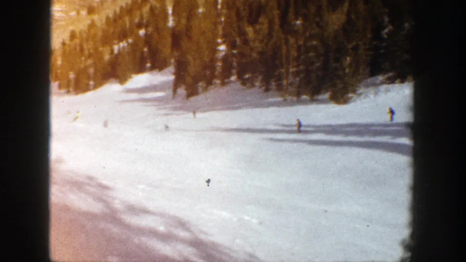 Several small skier figures traverse a bright 1961 Aspen snow slope while evergreen shadows stretch across the frame.