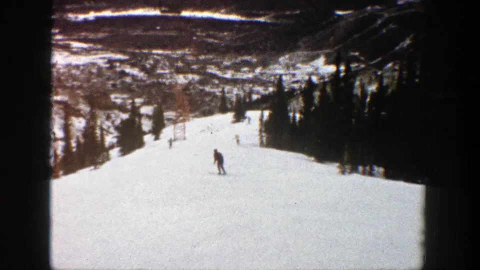 1961 Aspen ski footage frame with one skier crossing the open snow and a lift tower faintly visible uphill.