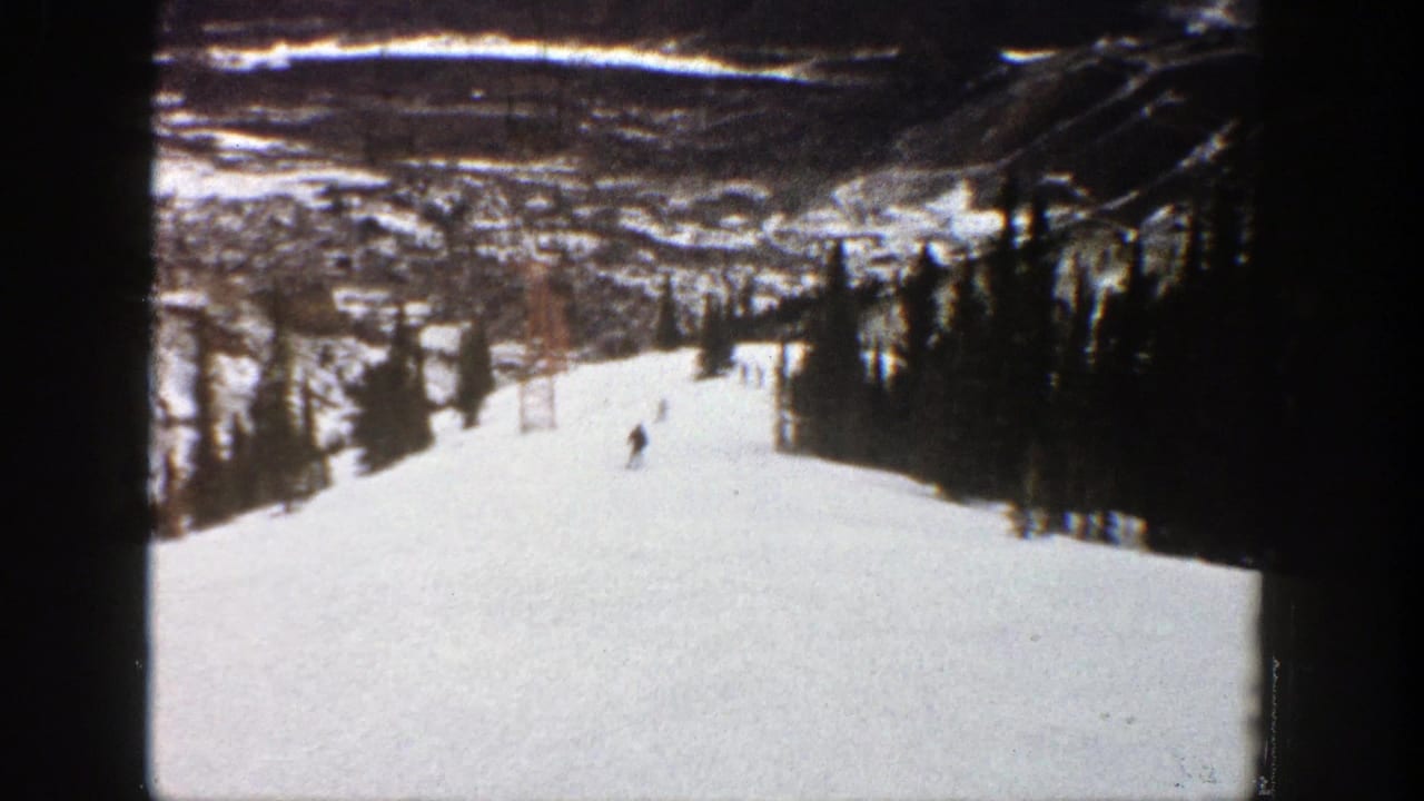 Snowy ski slope with small skiers, trees, distant valley, and dark film borders.
