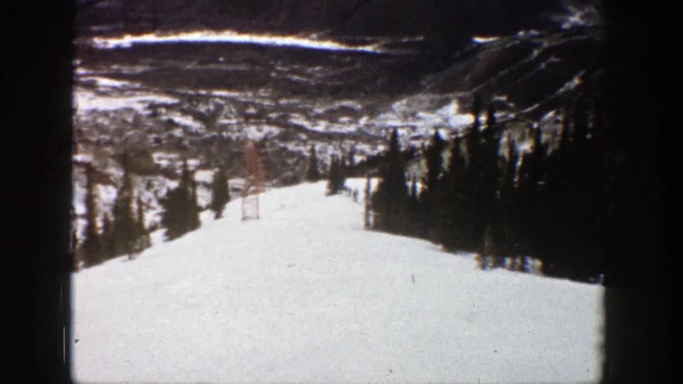 1961 Aspen, Colorado home-movie view of a snow-covered ski slope with evergreens, mountain terrain, and distant lift structures.