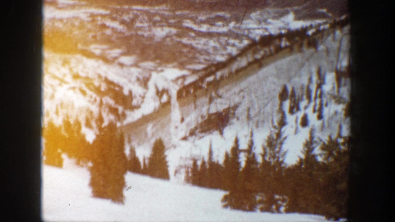 Snowy mountain slope with evergreen trees and a ski lift visible through dark film-frame borders.