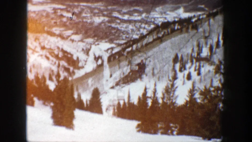 1961 Aspen winter resort view with a ski lift crossing a snow-covered slope above dark evergreen trees.