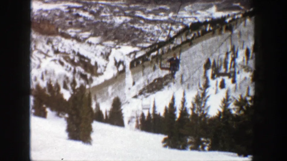 1961 Aspen 8mm frame showing a snowy resort slope with evergreens, lift equipment, and soft home-movie exposure.