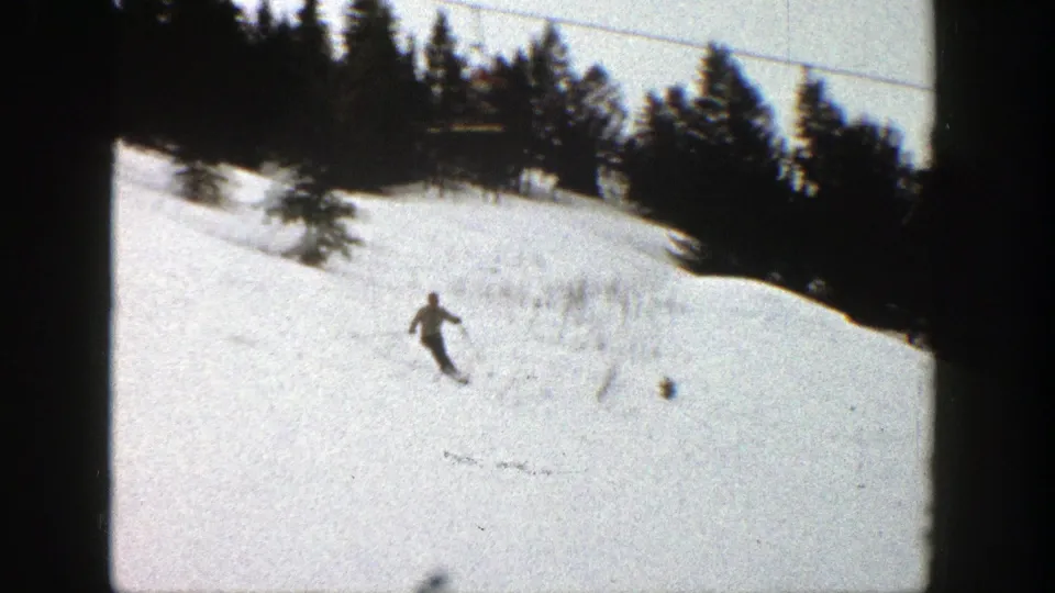1961 Aspen home-movie view of a distant skier moving downhill on a snowy slope with evergreens along the edge.