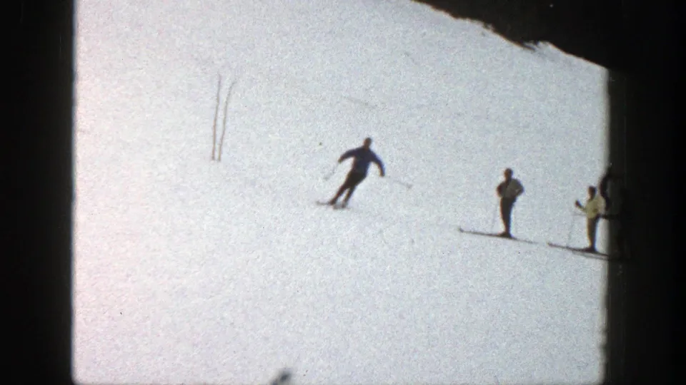 A skier glides across the Aspen slope while several distant people stand nearby on the snow.