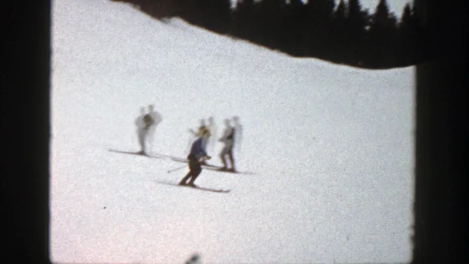 A small group of skiers stands on the Aspen slope while another skier crouches or glides below them.