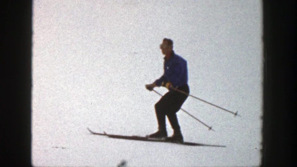 Closer 1961 Aspen 8mm frame showing the skier in a blue jacket bending at the knees while gliding on snow.