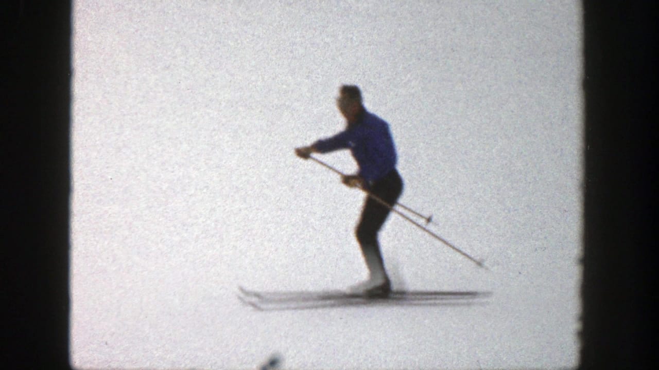 Adult skier in a blue coat gliding across a bright snowy slope.