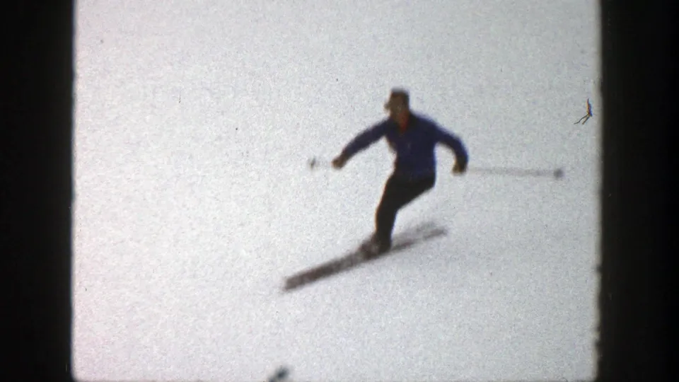 Adult skier turns downhill on a snowy Aspen slope, with motion blur and visible 8mm film edges.