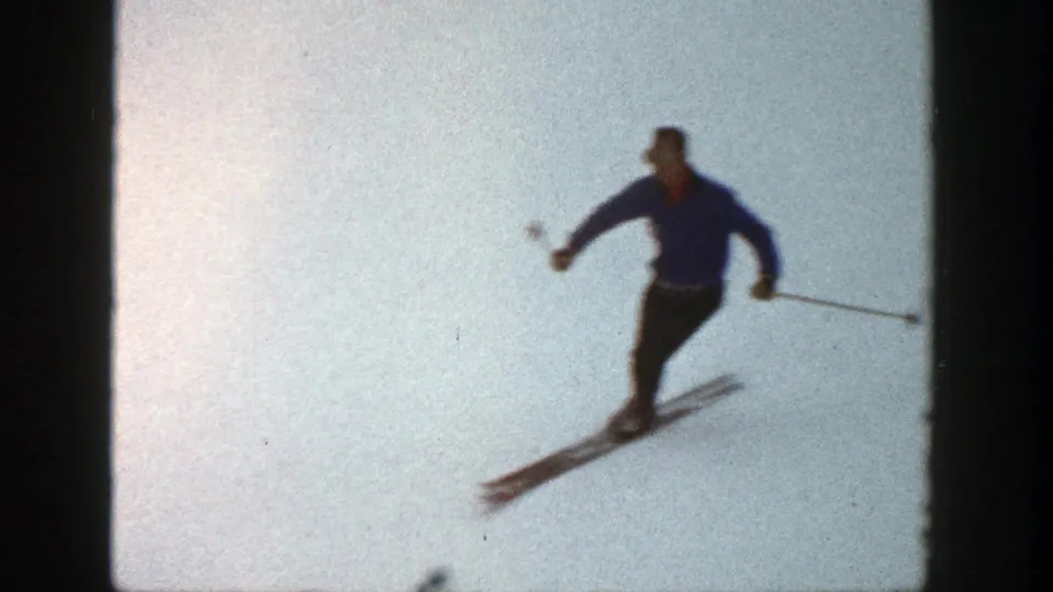 Adult skier in blue continues a downhill turn in the 1961 Aspen home-movie ski sequence.