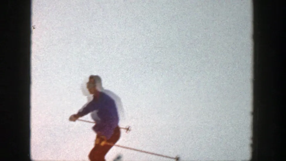Adult skier passes close to frame edge on the snowy Aspen slope, partly softened by home-movie blur.