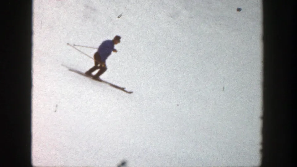 A skier in blue outerwear crosses the bright Aspen snowfield, framed by the exposed 8mm gate edges.