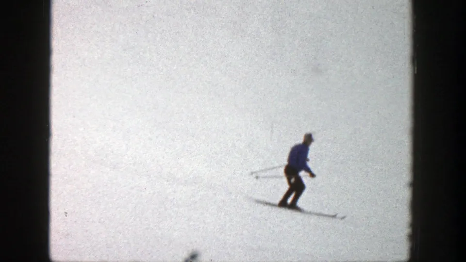 The Aspen skier appears smaller against the wide snow surface, continuing downhill in the 8mm home-movie frame.