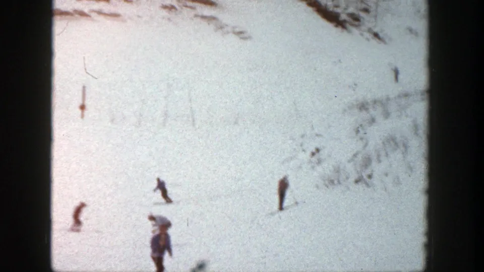 Aspen ski-slope frame with several small figures, faint tracks, and uneven snow texture in 1961 8mm footage.
