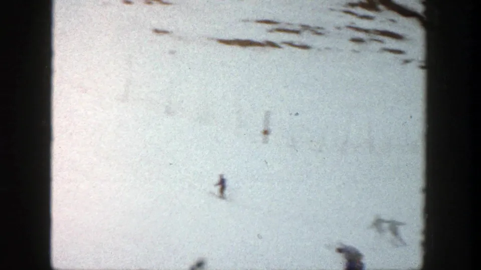 Wide 1961 Aspen home-movie view of a skier on an open snowy slope with other distant figures near the frame edge.
