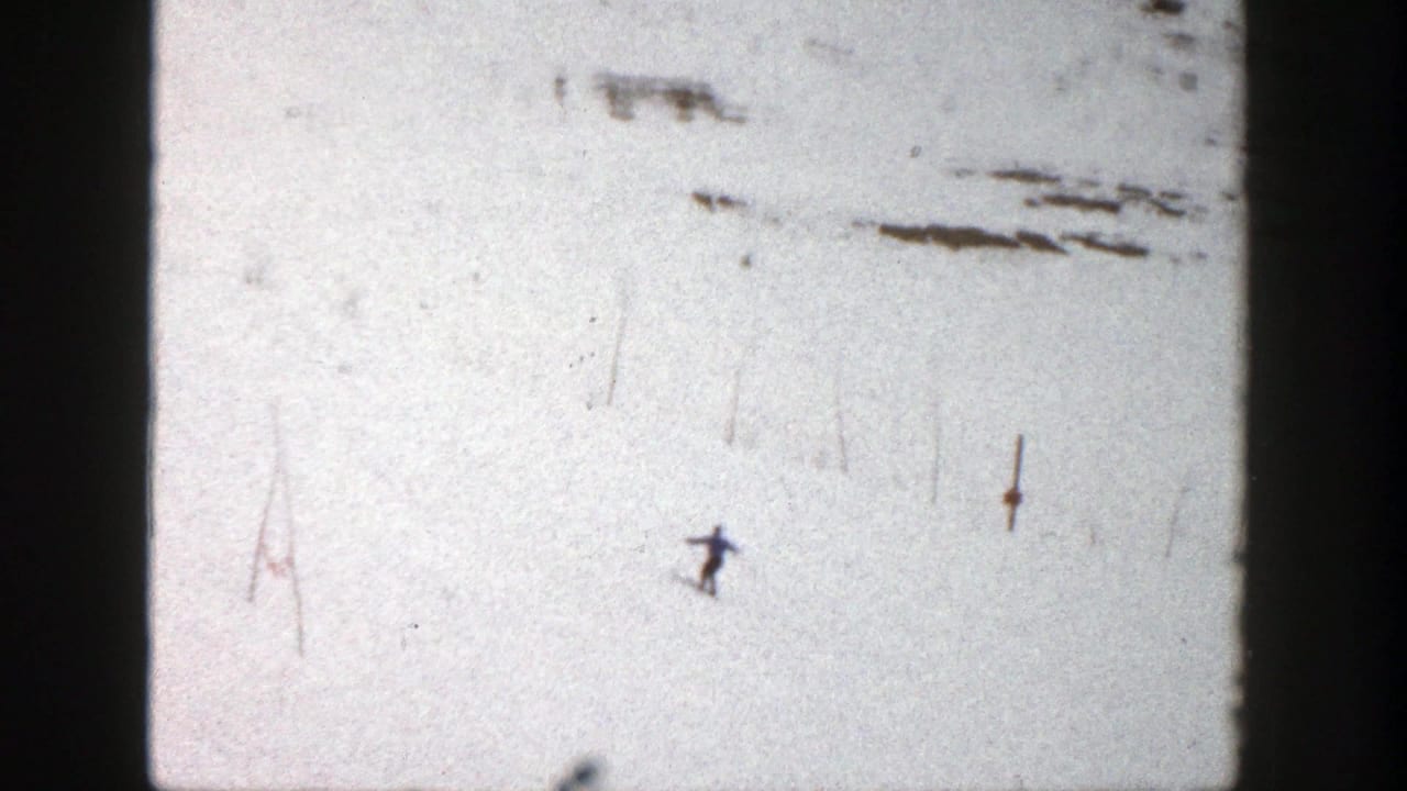 Distant skier on a bright snowy slope with dark film borders and surface marks.