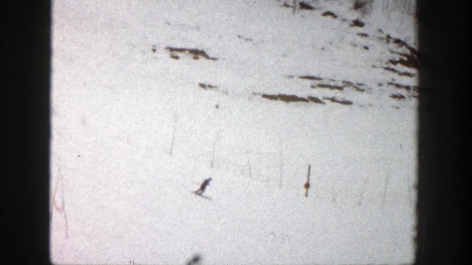 A distant skier appears on the bright Aspen snowfield, with dark exposed patches and visible 8mm film wear around the frame.