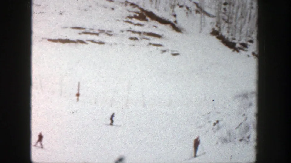 1961 Aspen ski-slope frame with a tiny skier on bright snow and another distant standing figure near the lower edge.
