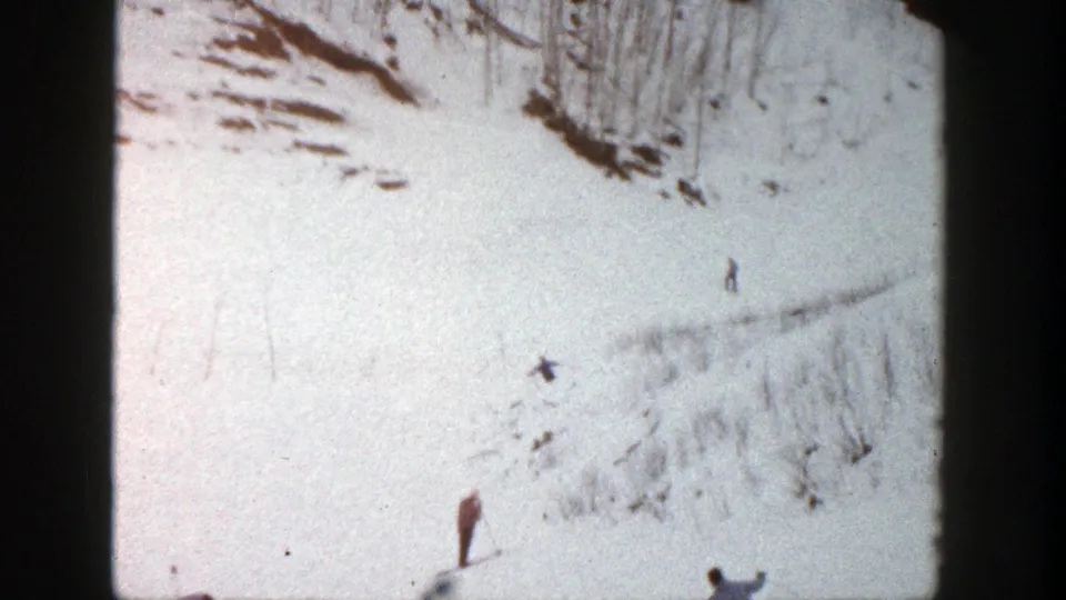 A distant skier crosses the Aspen snowfield as another figure stands near the lower frame edge, surrounded by visible 8mm grain and wear.